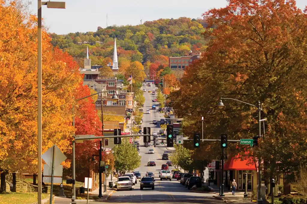 A busy, hilly downtown street lined with bright orange and yellow autumn trees and historic buildings.