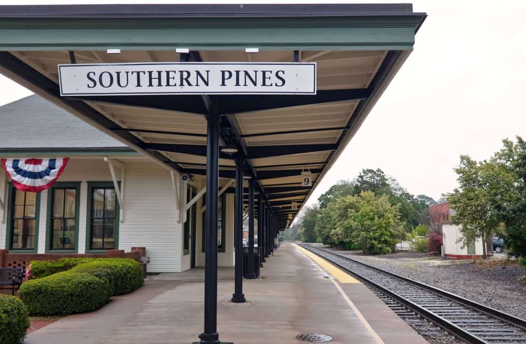 The historic Southern Pines railroad station featuring a covered platform, a town sign, and train tracks.